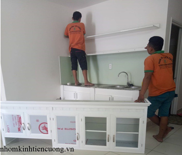 Thợ nhôm kính đang sửa bản lề tủ bếp bị xệ